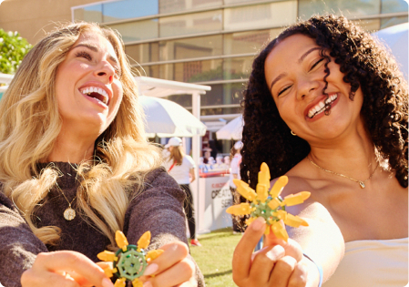 Two women laughing and holding crafted sunflowers